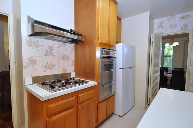 kitchen featuring stainless steel appliances, tasteful backsplash, a notable chandelier, and range hood