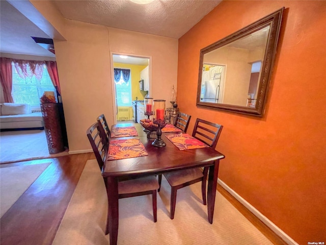 dining area with hardwood / wood-style floors, a textured ceiling, a healthy amount of sunlight, and radiator heating unit