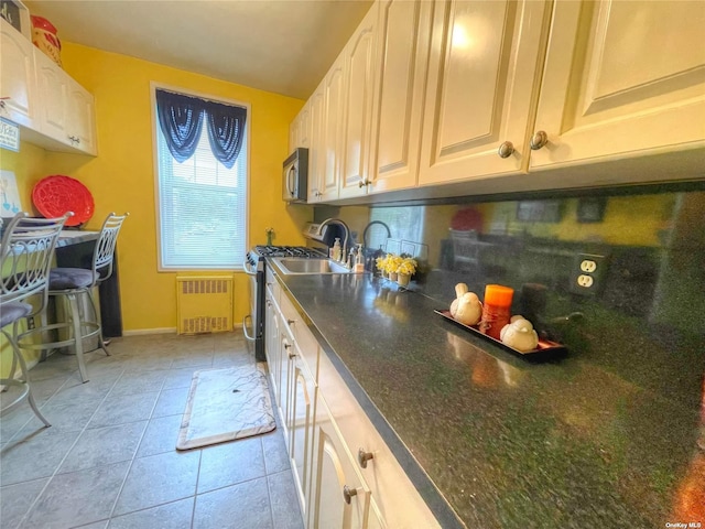 kitchen featuring white cabinets, light tile patterned flooring, stainless steel appliances, and radiator