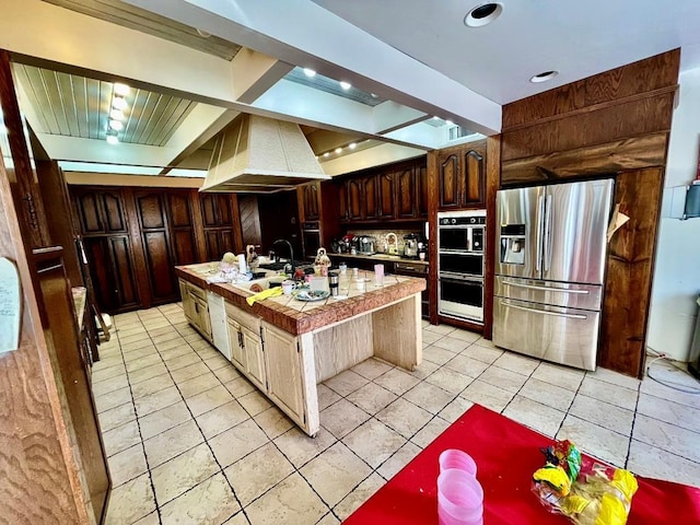 kitchen featuring custom exhaust hood, dark brown cabinetry, stainless steel appliances, sink, and an island with sink