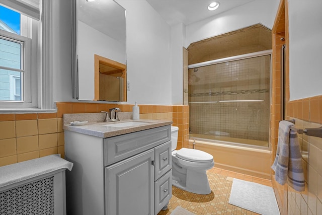 full bathroom featuring tile patterned floors, bath / shower combo with glass door, toilet, vanity, and tile walls