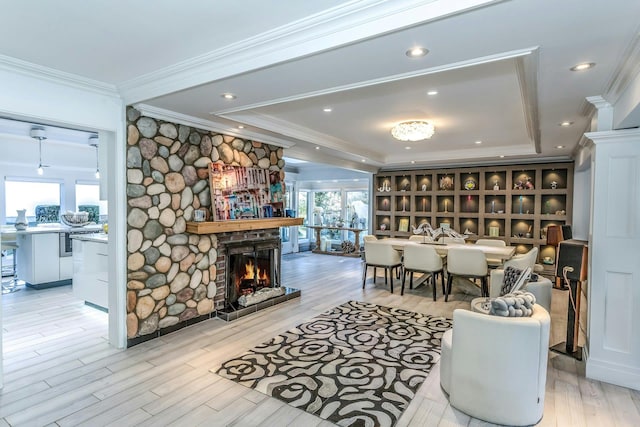 living room featuring ornamental molding, light hardwood / wood-style floors, a stone fireplace, and a tray ceiling