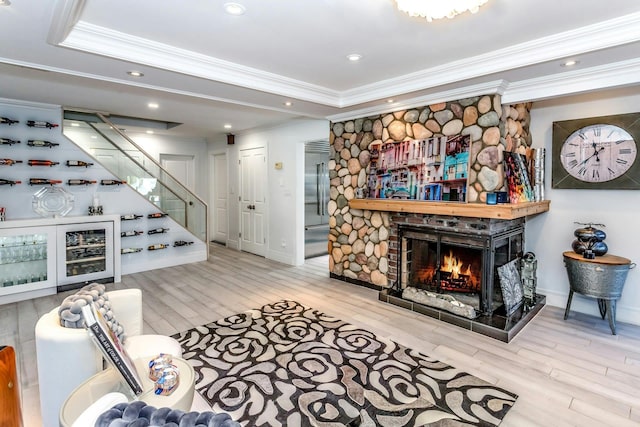 living room featuring wood-type flooring, a raised ceiling, ornamental molding, and a stone fireplace