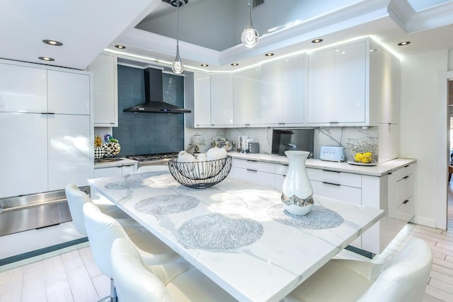 kitchen featuring refrigerator, wall chimney exhaust hood, hanging light fixtures, tasteful backsplash, and white cabinets