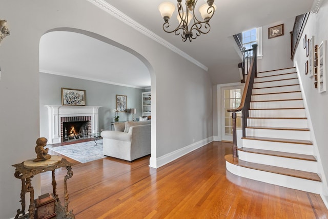 staircase with a brick fireplace, hardwood / wood-style flooring, crown molding, and an inviting chandelier