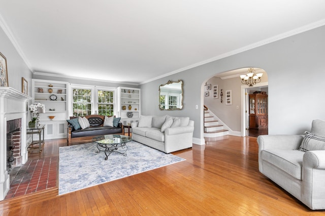 living room featuring a brick fireplace, ornamental molding, a chandelier, and wood-type flooring