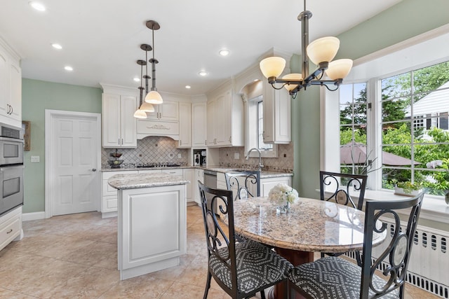 kitchen with radiator, a center island, white cabinetry, hanging light fixtures, and light stone counters