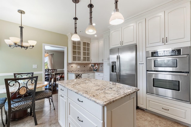 kitchen featuring white cabinets, a center island, stainless steel appliances, backsplash, and hanging light fixtures