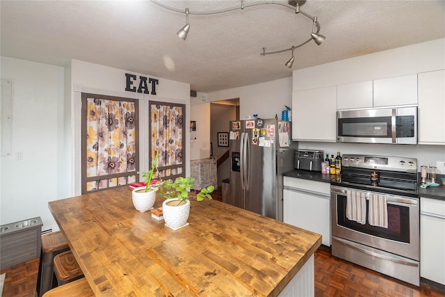 kitchen with a textured ceiling, white cabinets, stainless steel appliances, and wood counters