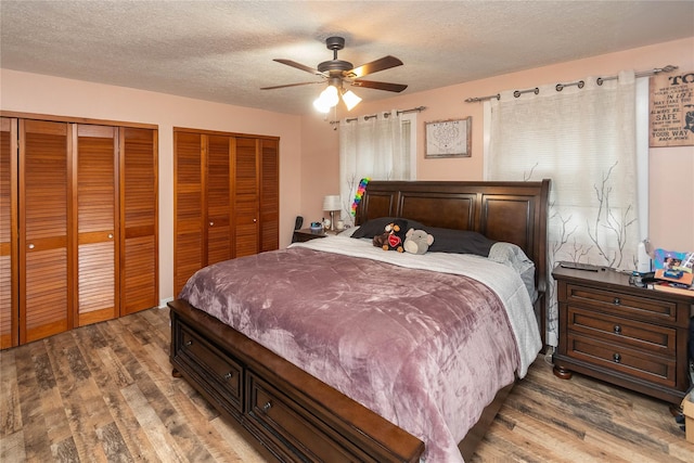 bedroom with ceiling fan, two closets, a textured ceiling, and hardwood / wood-style floors