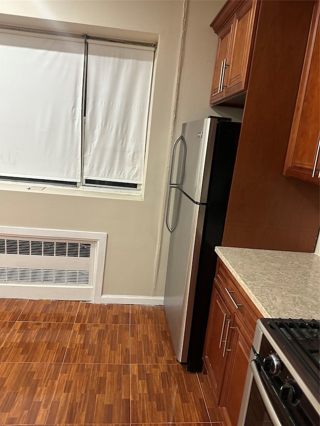 kitchen featuring dark wood-style flooring, brown cabinets, radiator, light countertops, and appliances with stainless steel finishes