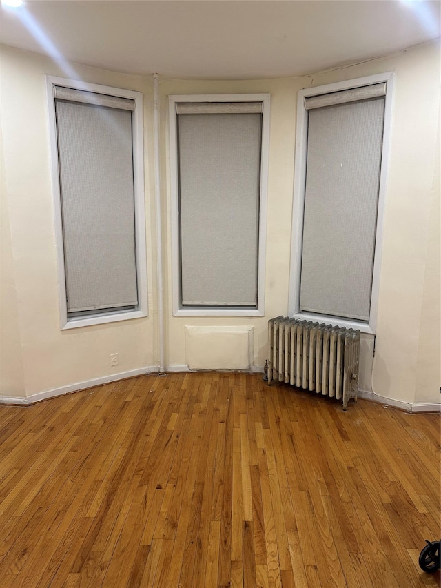 empty room featuring wood-type flooring, baseboards, and radiator heating unit