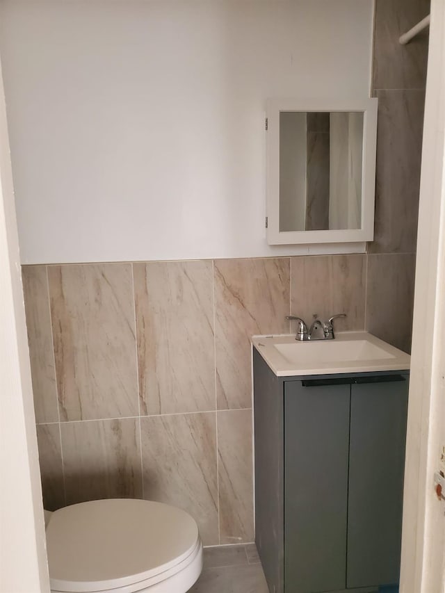 bathroom featuring toilet, vanity, and tile walls