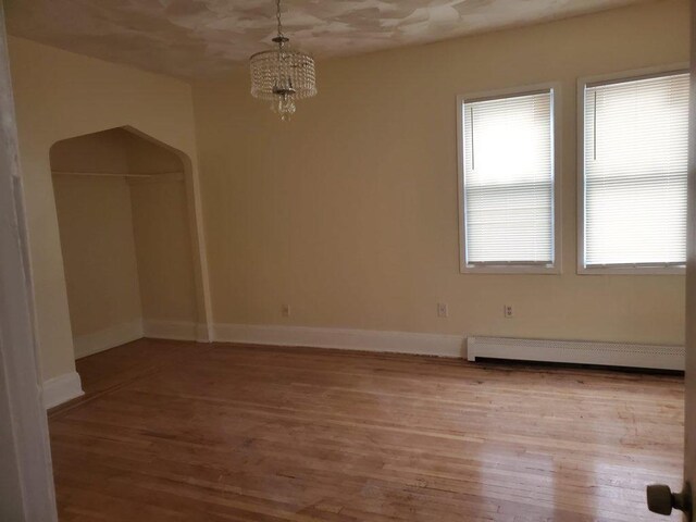 spare room featuring baseboard heating, light wood-type flooring, and a chandelier