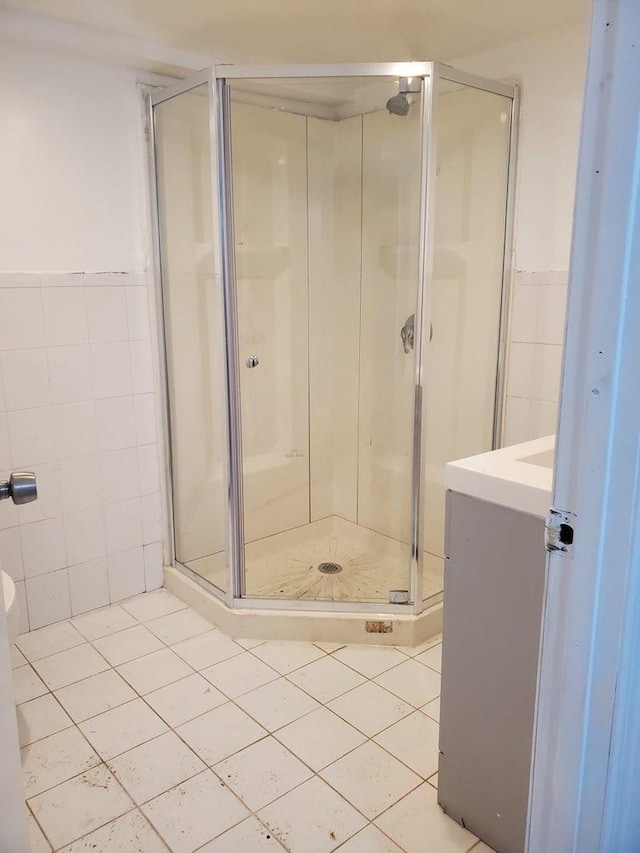 bathroom with a shower with door, vanity, tile walls, and tile patterned floors