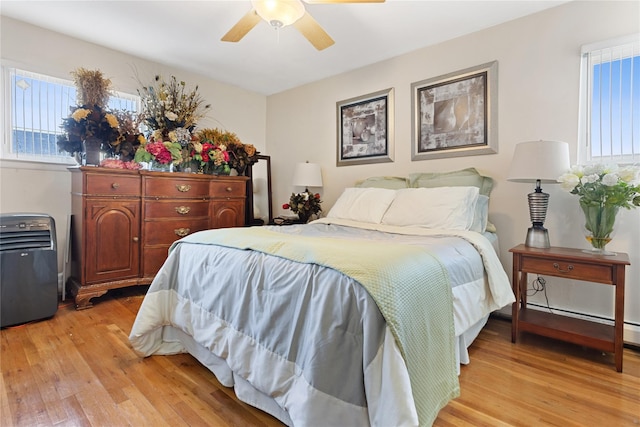 bedroom featuring ceiling fan, a baseboard heating unit, and light wood-type flooring