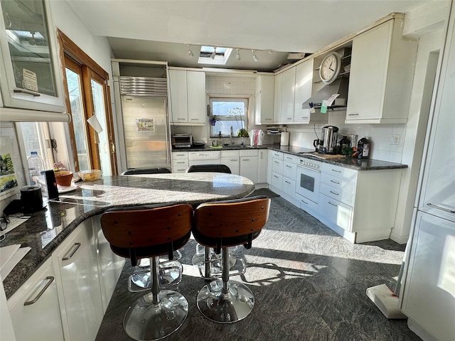 kitchen with white cabinetry, plenty of natural light, stainless steel built in fridge, wall chimney range hood, and sink