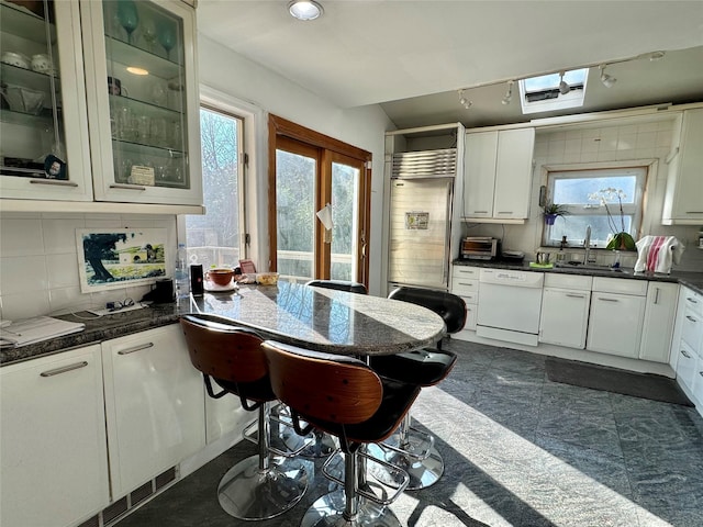 kitchen with white dishwasher, white cabinetry, decorative backsplash, and a skylight