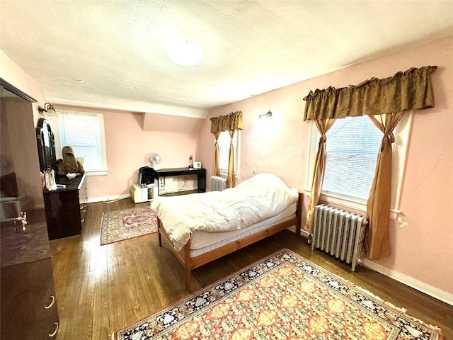 bedroom featuring dark hardwood / wood-style floors, radiator heating unit, and multiple windows