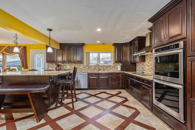 kitchen featuring appliances with stainless steel finishes, a wealth of natural light, pendant lighting, and wall chimney range hood