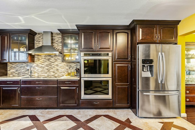 kitchen featuring tasteful backsplash, dark brown cabinets, wall chimney exhaust hood, and stainless steel appliances