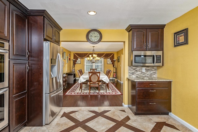 kitchen featuring tasteful backsplash, dark brown cabinetry, stainless steel appliances, and an inviting chandelier