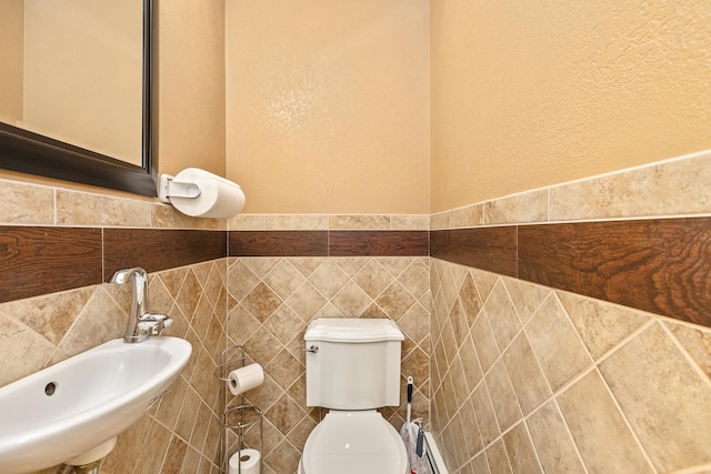 bathroom with baseboard heating, sink, tile walls, and toilet