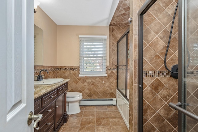 full bathroom featuring combined bath / shower with glass door, vanity, a baseboard heating unit, tile walls, and toilet