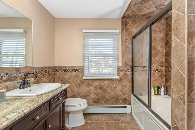 full bathroom featuring combined bath / shower with glass door, vanity, baseboard heating, tile walls, and toilet