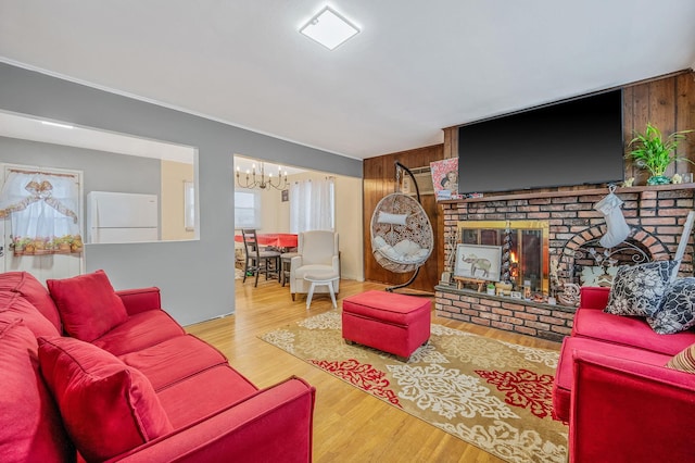 living room featuring hardwood / wood-style floors, an inviting chandelier, wooden walls, and a brick fireplace