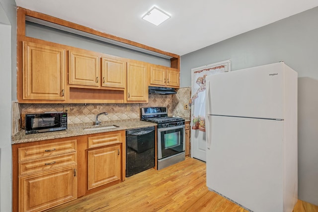 kitchen with backsplash, light stone counters, sink, black appliances, and light hardwood / wood-style floors