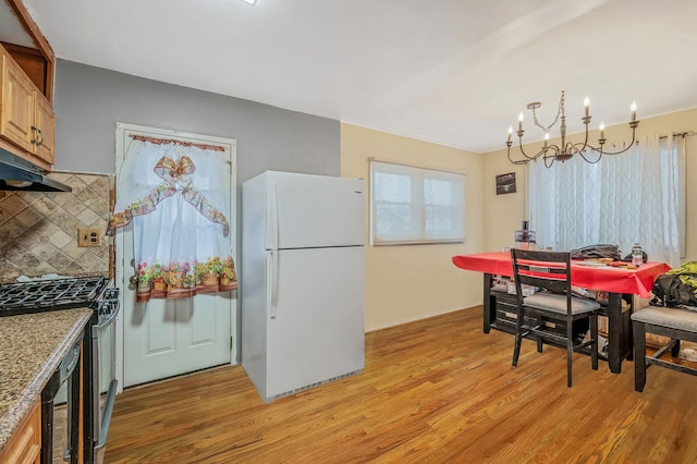 kitchen featuring a notable chandelier, white fridge, stainless steel range with gas stovetop, decorative backsplash, and light wood-type flooring