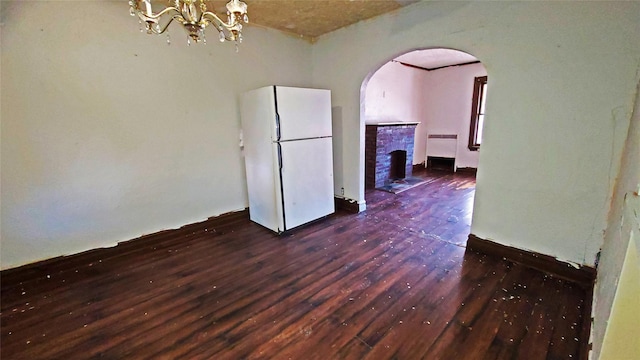 spare room featuring a notable chandelier, dark hardwood / wood-style floors, radiator heating unit, and a brick fireplace