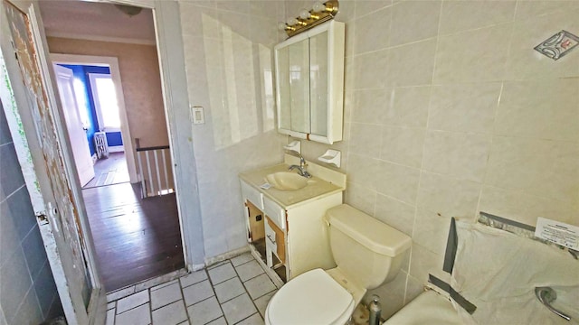 bathroom featuring tile patterned floors, vanity, tile walls, radiator heating unit, and toilet