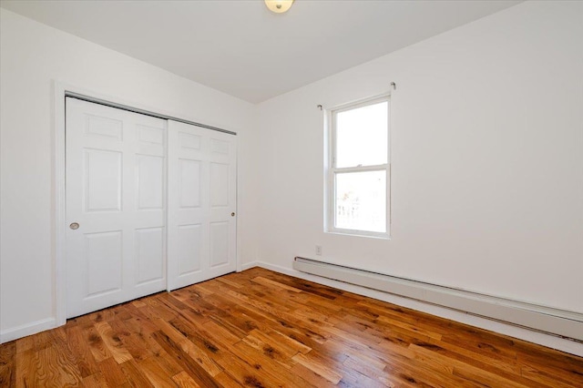 unfurnished bedroom featuring hardwood / wood-style floors, a closet, and a baseboard radiator