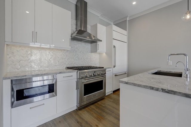 kitchen with high quality appliances, white cabinetry, sink, hanging light fixtures, and wall chimney exhaust hood