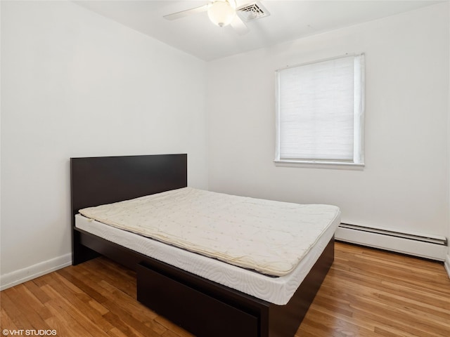 bedroom featuring ceiling fan, a baseboard heating unit, and hardwood / wood-style floors