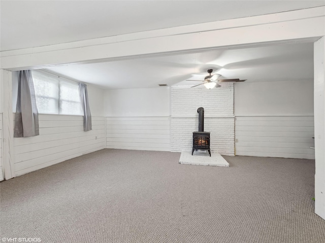 unfurnished living room with carpet floors, a wood stove, wood walls, and ceiling fan