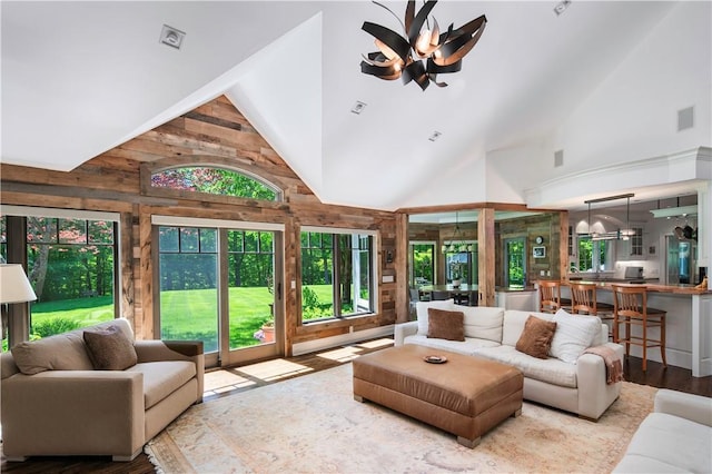 living room with a notable chandelier, light hardwood / wood-style flooring, high vaulted ceiling, and wood walls