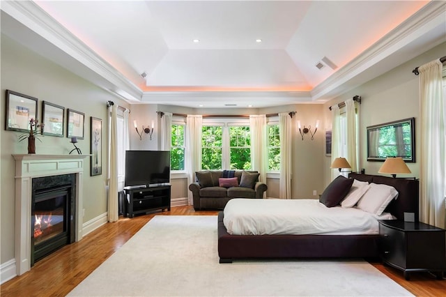 bedroom featuring a premium fireplace, light wood-type flooring, and a tray ceiling