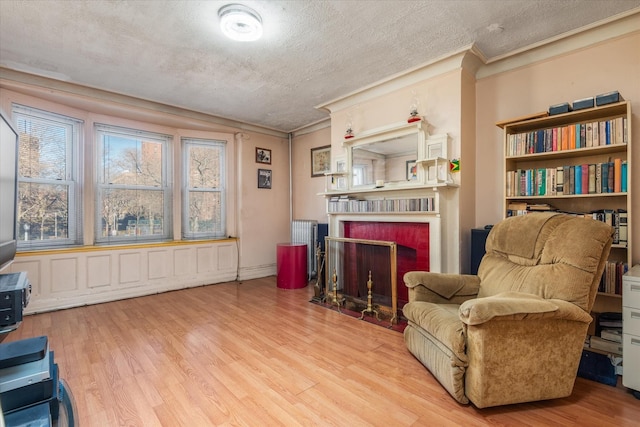 living area featuring a fireplace, a textured ceiling, light hardwood / wood-style flooring, and crown molding