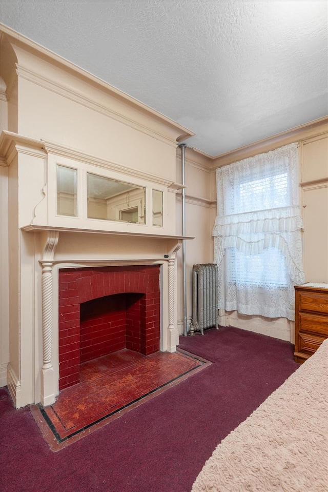 unfurnished bedroom with radiator heating unit, a brick fireplace, crown molding, a textured ceiling, and dark carpet