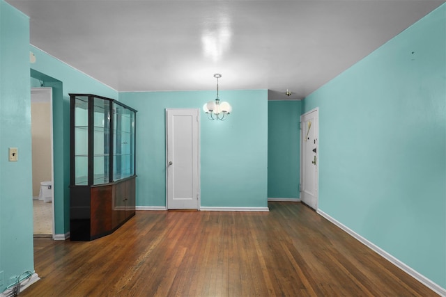 spare room with dark hardwood / wood-style flooring and an inviting chandelier