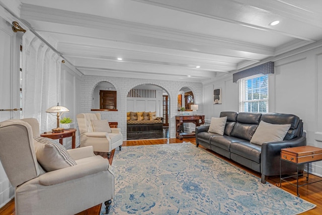 living room featuring crown molding, beam ceiling, a fireplace, wood-type flooring, and brick wall