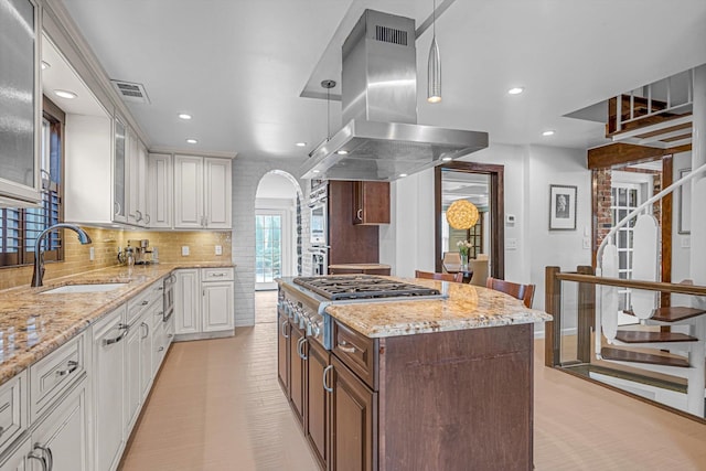 kitchen featuring stainless steel gas cooktop, sink, white cabinetry, island range hood, and a center island