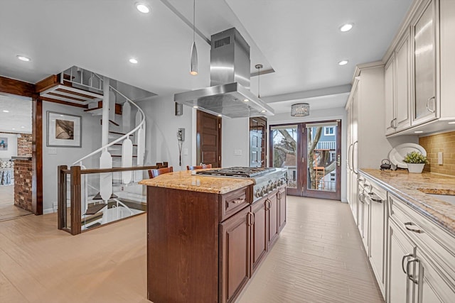 kitchen with light stone counters, island exhaust hood, decorative backsplash, and hanging light fixtures