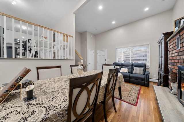 dining area featuring a high ceiling, light hardwood / wood-style floors, a brick fireplace, and a baseboard heating unit