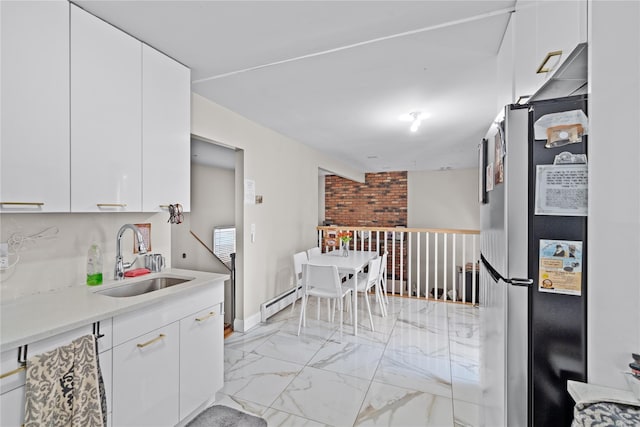 kitchen with baseboard heating, stainless steel refrigerator, white cabinetry, and sink