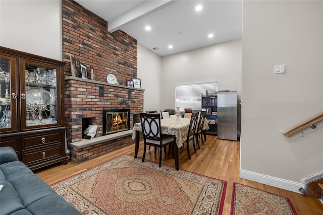 dining area featuring beam ceiling, light hardwood / wood-style floors, and a brick fireplace