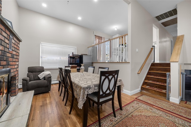 dining space featuring hardwood / wood-style flooring, a brick fireplace, and a baseboard heating unit